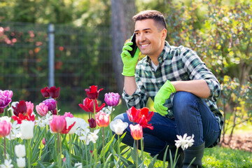 gardening and people concept - happy smiling middle-aged man with flowers calling on smartphone at summer garden