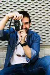 Bearded traveler man sitting on ground while using checking a camera