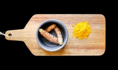 Turmeric root in bowl and spice powder on a cutting board