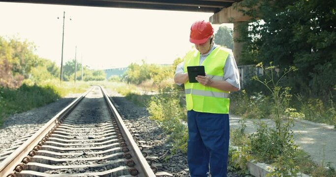 Senior railroader in uniform using tablet when checking serviceability of rails