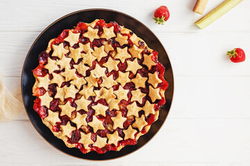 Strawberry and rhubarb pie decorated with stars on white table, top view