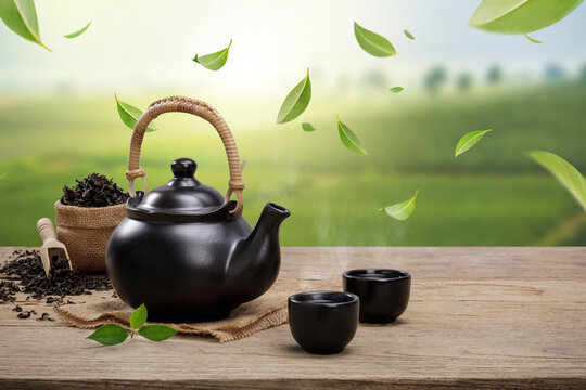 Cup of hot tea with teapot, flying green tea leaves in the air and dried herbs on the wooden table in plantations background, Organic product from the nature for healthy with traditional