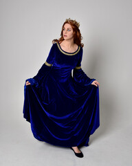 Naklejka premium Full length portrait of girl wearing long blue velvet gown with golden crown. standing pose with back to the camera, isolated against a studio background.