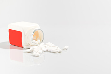 Vitamin tablets are separated from a red-white bottle on a white background. There is copy space for your messages.