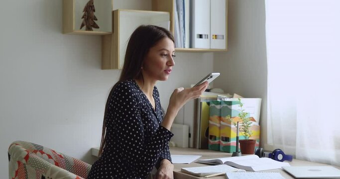 Woman sit at desk hold phone use virtual assistant answer questions while studying, make requests on internet services search. Girl send voice message, capabilities of modern smartphones usage concept