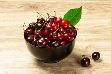Ripe cherries in black bowl on wood background