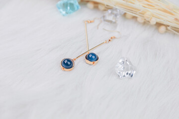  Close-up of blue metal earrings.Made of blue round beads and golden yellow metal.  Down blankets and beautiful dried flowers are used as decorations.  Transparent ice cube props.