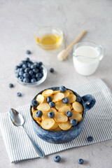 Blue Bowl of mini pancake cereal with blueberries, maple syrup and milk on concrete background. Tiny pancakes, new food trend concept. Cute healthy breakfast or snack. Recipe, menu.