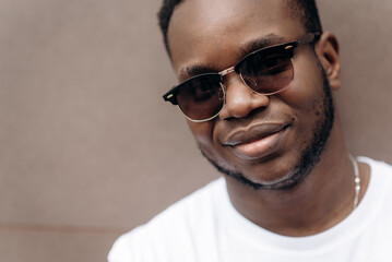 Obraz premium Close up male portrait. Handsome african american guy in a white t-shirt and in sunglasses posing and smiling