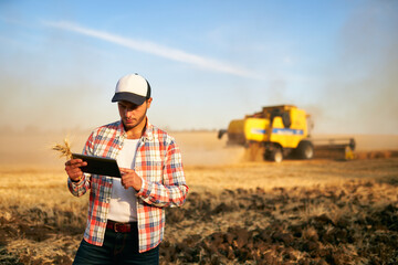 Precision farming. Farmer holding tablet for combine harvester guidance and control with modern...