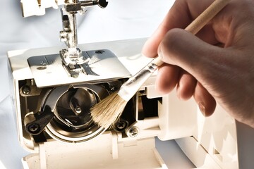 Cleaning and preparation of sewing machine. A woman uses a brush to clean the inside of the sewing machine from dust.