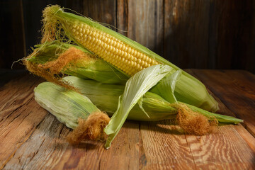 ripe ears of sweet corn close-up on a wooden table, horizontal view, rustic style