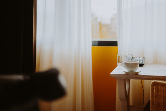 Blick in ein Zimmer mit Tisch Kaffeetasse und Telefon im Hintergrund ein Fenster mit Vorhängen