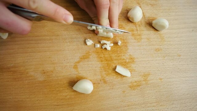 Cut garlic with a knife. Woman cuts the cloves of garlic on small pieces.