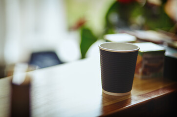 Disposable coffee paper cup on bar counter. Morning light falls from the window.Coffee break.Blurred image,selective focus