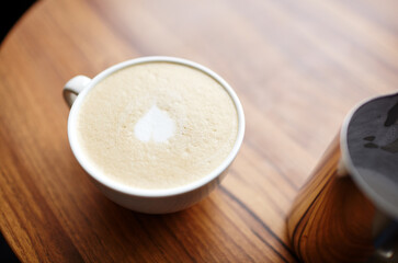 Milk jug and cup of coffee latte on table in cafe. Morning light falls from the window.Coffee break.Blurred image,selective focus