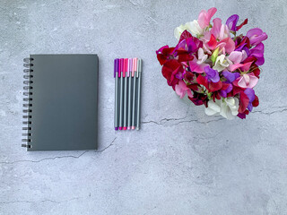 Bouquet sweet peas, note book, pencils gray grungy background. Minimalist design, photography from...