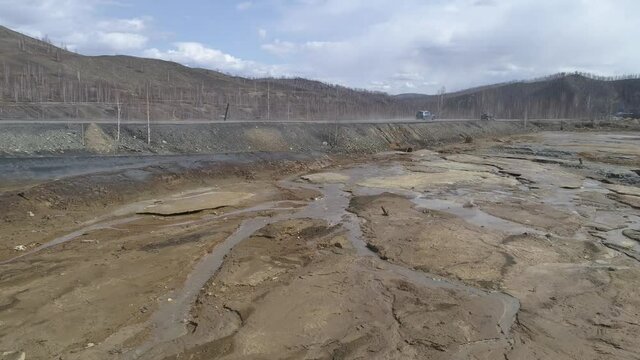 Aerial view of dry riverbed poisoned by copper production in Karabash city. Near the road. Cars are driving along the road. Spring cloudy day. Russia, Chelyabinsk region
