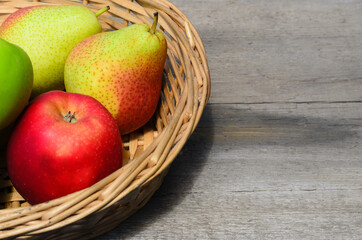 Apples and pears in a wicker basket on a rough wooden table.