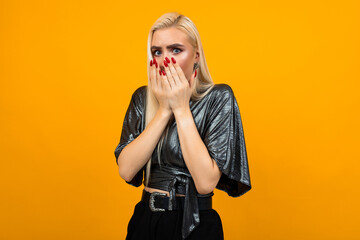 portrait of a blond startled young woman covering her face with hands on a yellow studio background