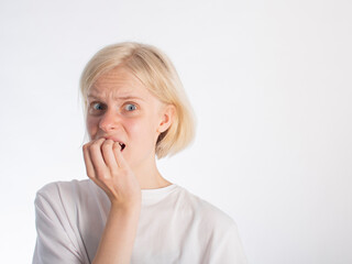 a young blonde girl in a white t-shirt bites her fingernails due to stress/excitement. isolate on white. space for text