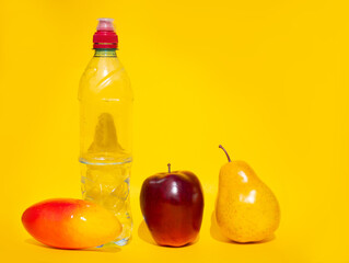 Fresh and healthy fruits: red Apple, yellow pear and mango lie on a yellow background next to a sports water bottle. Concept of proper nutrition, place for text