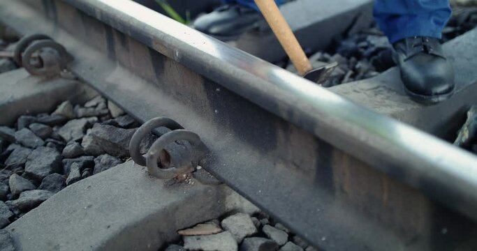 Close low view of railroader checks the rails serviceability with hammer