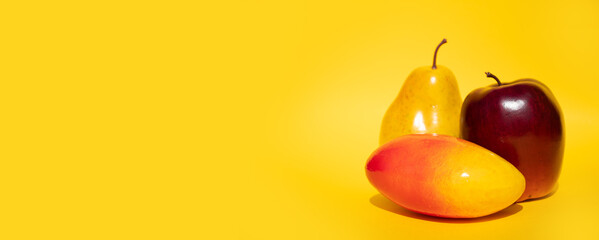 Fresh fruit: red Apple, yellow pear and mango lie on a yellow background. Place for text, healthy food concept