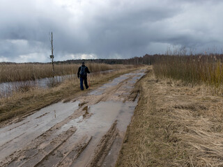 a human figure on a dirty dirt road, old reeds on the side of the road, spring view