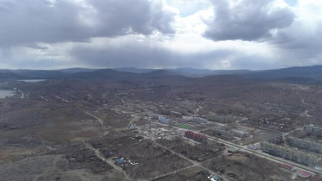 Aerial view of Karabash city with five-story houses and church. Cars drive along the road. Empty streets. Spring, trees without leaves. At the background the Ural mountains. Russia, Chelyabinsk region