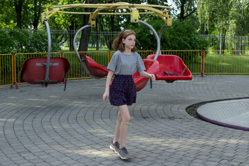 A teenage girl got up from the carousel in an amusement park and wants to leave. Alone in the park, single visitor, social distancing.