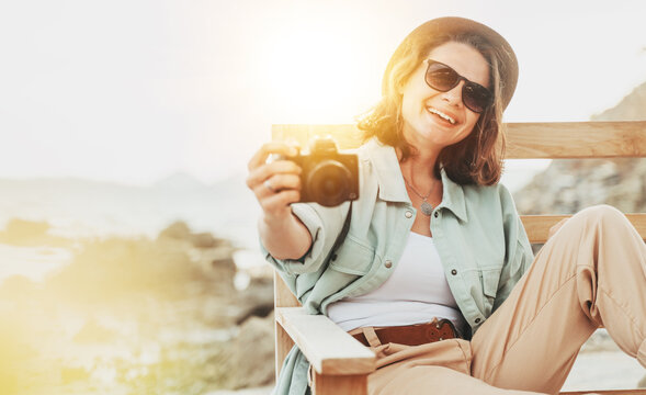 Outdoor summer smiling lifestyle portrait of pretty young woman having fun in with camera travel photo of photographer Making pictures in hipster style glasses and hat