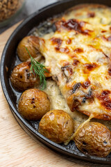 Mouthwatering pub dish in cast iron: baked baby potato with poultry and cheese crust