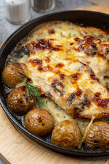 Mouthwatering pub dish in cast iron: baked baby potato with poultry and cheese crust