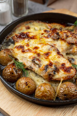 Mouthwatering pub dish, cast iron: baked baby potato with chicken and cheese crust, very close up