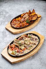 Cast-iron, oven baked meals: vegetable ragout and meat with potato in spicy gravy, two cast-iron trays on grey concrete table