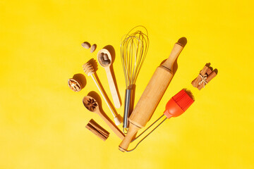 Kitchen items for cooking. Whisk, wooden spoons, nuts and cinnamon on a yellow background