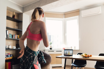 Young woman dancing at home following video lesson on the laptop. Pretty female repeating exercises while watching online workout session.