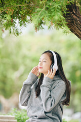 Beautiful young Vietnamese teenage girl smiling and closing eyes when listening to her favorite music in headphones