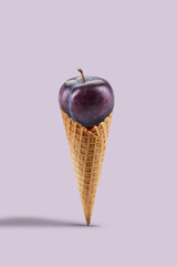 Ripe purple plum in a sweet wafer cone against lilac background. Healthy nutrition, seasonal harvest of fruits. Close up, copy space