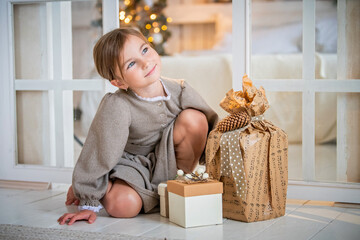 child, a girl of primary school age in a bright interior, examines boxes with gifts on the...