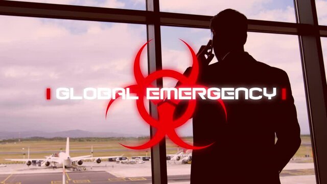 Hazard sign with Global emergency text against man talking on smartphone at airport