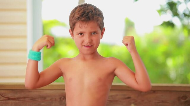 The confident-looking boy is showing muscles outdoors on the porch