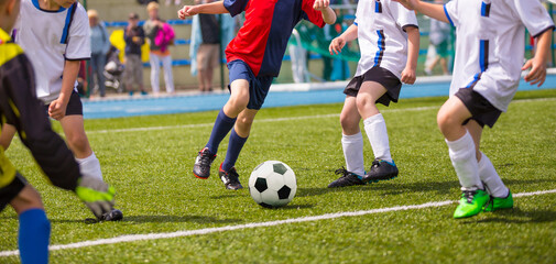 Obraz premium Young Athletes Kicking Soccer Ball on Wet Grass Field. Youth Football Players In Run Duel. Children Kicking Sports Game at School Field. Kids Level Soccer Tournament