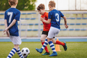 Obraz premium Youth Junior Athletes in Red and Blue Soccer Shirts. Sports Education. Kids Football Players Kicking Ball on Soccer Field. Sports Soccer Horizontal Background. Spectators on Stadium in the Background