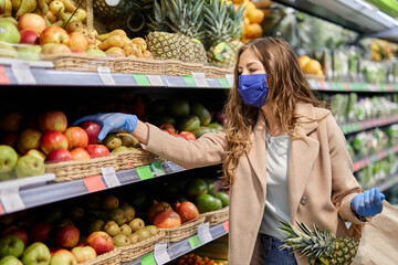 Healthy fruits with vitamins during the coronavirus Covid-19 pandemic. Woman in facial mask and rubber gloves buys fruit at market.