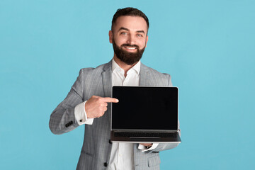 Positive entrepreneur with laptop pointing at empty screen with space for your design over blue background