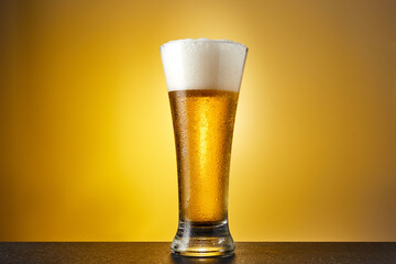 Cold craft light Beer in a glass with drops on a dark table. Pint of Beer on yellow color background.