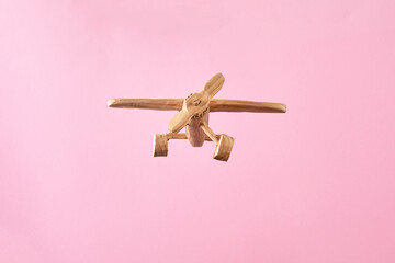 Handmade wooden airplane toy flying on a pastel pink background.