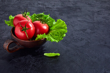 Fresh grape tomatoes with salad Leaves on black stone background. Vegan veggies diet food. Herb, red tomatoes, cooking concept.